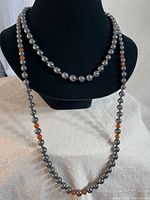 Full view of both hematite necklaces on display stand, one long with amber beads and one short choker with large hematite beads.