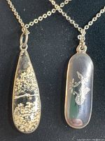 Front view of two sterling silver pendants with etched stone and enameled marque, both on chains