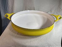 Front view of yellow enamel paella pan with white interior and yellow handles