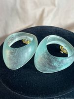 Top-front view of the pair of light green-blue chunky earrings showing frosted curved surface and clip-on backs.
