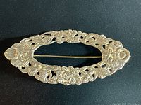 Top view showing the full elongated oval brooch with detailed floral and leaf pattern in raised relief and open spaces.