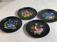 Four vintage Bakelite coasters arranged showing variety of floral hand painted designs on black background