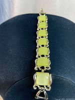 Full view of vintage lime green Lucite bracelet laid out on black display, showing square Lucite stones with gold-tone curled edges set in series.