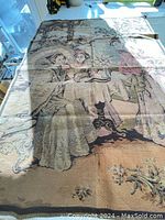 Full view of vintage woven textile panel showing three figures in kimono around a table with vase of flowers and architectural backdrop.