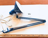 Full view of vintage blue Luxo Activist clamp lamp with extended adjustable swing arm, clamp base, power cord, plug, and white interior reflector.