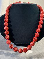 Full view of the necklace displayed on a black bust, showing the full length and shape of the necklace composed of round cinnabar carved beads.