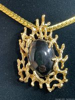 Close-up of the brooch pendant showing large black oval stone and detailed gold tone textured frame.