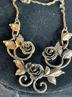 Close-up view of the necklace front showing three dimensional roses and leaves with swirling vine pattern.