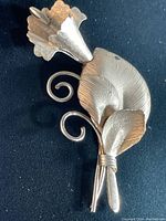 Close-up photo showing the detailed front floral design of the sterling brooch, featuring textured leaves, flower petals, and curled stems in silver metal, displaying its vintage craftsmanship.