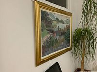 Side view of the large framed oil painting showing its gold frame and hanging orientation near a plant.