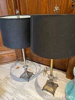 Photo showing two lamps side by side, highlighting their different metal base finishes and black fabric shades.
