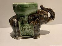 Side view of the ceramic elephant planter showing brown-black glossy glaze with green saddle and planter bowl.