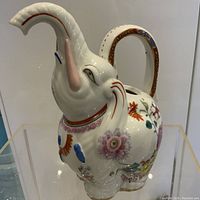 Porcelain elephant water jug with raised trunk as spout, decorated with floral and ornamental patterns in multiple colors.