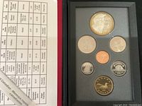 Top-down image showing six coins in protective foam, including larger silver dollar and smaller denominations with proof finish, alongside detailed coin specifications sheet.
