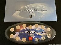 Top view of open display case showcasing 24 silver Canadian quarter coins from the millennium series arranged around a map of Earth with millennium text and logos.