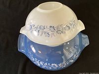 Top-down view of two nested Pyrex Cinderella mixing bowls showing white bowl on top of blue bowl with floral patterns.