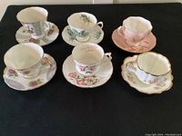 Overview of six cups with saucers showing variety of floral designs, lustre ware finishes, and pastel colors