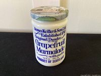 Front view of white milk glass marmalade jar with blue text and original decorative metal lid.