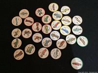 Top-down view of 31 colorful circular plastic tokens with various vintage car images showing years from early 1900s to 1920s, some with wear and one chip noted on a token with Hudson #148.