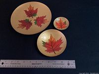 All three dishes displayed with ruler for scale on dark background, showing large oval dish with three maple leaves, medium round dish, and small round dish