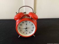 Front view of red double bell wind up alarm clock showing the dial and bells.
