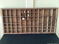Front view of the wooden miniatures display shelf showing all compartments and a few miniatures inside.