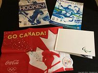 Photo showing hockey guide, event guide, red and white Canadian flag with hockey silhouette and Coca-Cola Olympic branding, folded booklet, and circular 2010 pin.