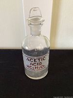 Full view of the clear Pyrex apothecary bottle with reddish brown etched label 'Acetic Acid HC2H3O2'.