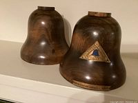 Pair of wooden bell-shaped bookends with metal plaques and base labels, showing front and angled views