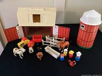 Full set overview showing red and white barn with doors open, silo, tractor, animal figures, fences, feeding trough, and Little People farmers.