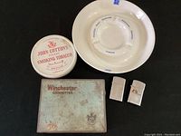 Zippo lighters, tobacco tins, and ceramic ashtray displayed together on black surface