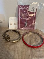 Photo shows American Girl Doll keepsake charm in packaging, fried egg shaped stud earrings on card, and two bracelets - one metal with floral accent and one red rhinestone bangle.
