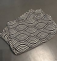 Photo of a folded black and white throw blanket showing a wave-like geometric pattern on a smooth surface.