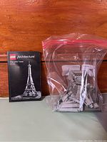 Photo showing Lego Architecture Eiffel Tower instruction manual and loose pieces in a plastic bag on a wooden surface.
