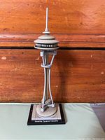 Photo shows Lego Architecture Seattle Space Needle model with its black rectangular base labeled 'Seattle Space Needle'. The model is made of mostly gray pieces, detailed with round observation deck and antenna spire, supported by three angled legs.