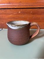 Side view of a brown ceramic mug with a smooth white interior and a curved handle.