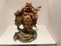 Front view of the Laughing Buddha statue showing smiling face, robe folds, gold ingot, coins, and sack.