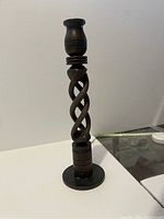 Photo of dark wooden twisted design candlestick standing upright on a surface.