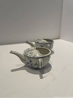 Two white porcelain moustache cups with blue floral pattern and spouts, shown from side profile.