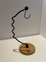 Banana holder with black metal wavy stand and wooden round base, shown on white surface with shadow cast.