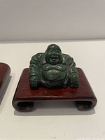 Laughing Buddha statue seated on a carved reddish wooden stand with curled legs