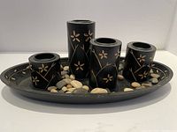 Photo of four black floral candle holders on an oval black tray surrounded by smooth decorative stones.
