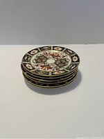 Stack of six 6-inch Crown Derby Imari porcelain plates showing detailed floral and geometric pattern with gold trim