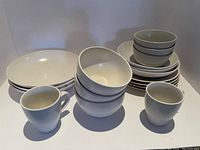Stack of various white dishes including large plates, smaller plates, bowls, and mugs.