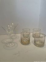 Two clear martini glasses and four short decorated drinking glasses against a white background.