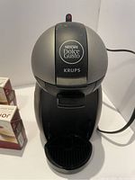 Photo showing the Krups Nescafe Dolce Gusto coffee machine with various coffee pods beside it.