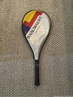 Tennis racket inside a zippered protective cover labeled SNAUWAERT with a colorful design in red, yellow, blue, and silver.