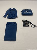 Four items laid out on white background: blue Barbie skirt, matching blue jacket, black purse with strap, blue American Airlines carry bag.