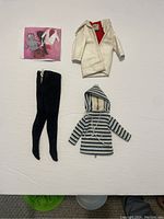 Top-down view of vintage Barbie clothing including coat, stockings, striped hooded jacket, and accessory card