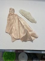 Peach satin evening dress with attached cape and white faux fur stole laid flat on white surface